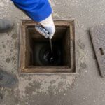Radnik proverava unutrašnjost otvorenog kanalizacionog šahta pomoću sajle tokom pregleda i održavanja kanalizacije.