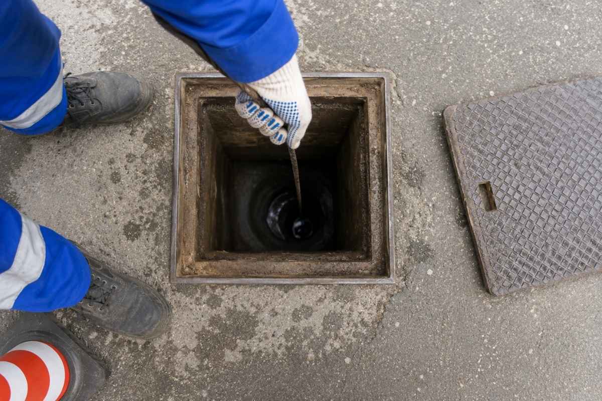Radnik proverava unutrašnjost otvorenog kanalizacionog šahta pomoću sajle tokom pregleda i održavanja kanalizacije.